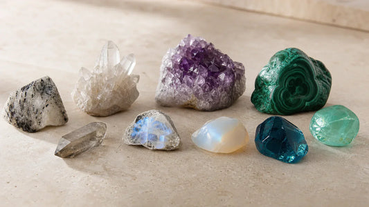 Natural gemstone crystals beside glass and resin look-alikes on a cream stone surface.